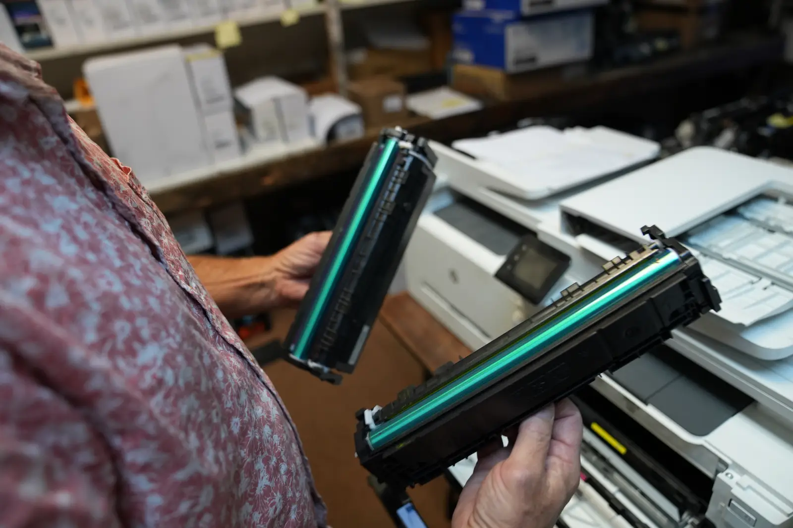Hands holding two laser printer drum cartridges beside an open printer